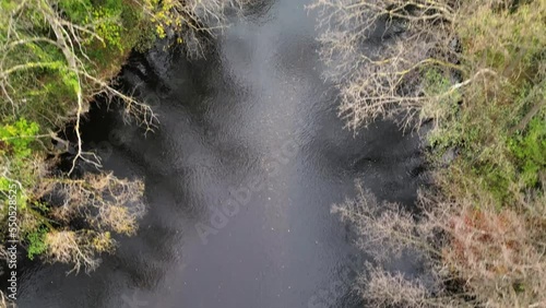 Flying upward shot of the Rur river in Kreuzau, Germany during a cold Autumn afternoon next to a pathway and farm fields with a view of a small walkover bridge photo