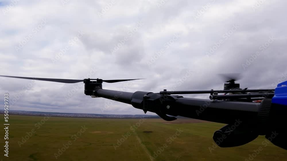 Rotating propellers of the drone against the background of an overcast sky. The drone flies over the green field of the airfield. Flying drone, top view Rotating propellers of the drone against the background of an overcast sky. The drone flies over the green field of the airfield. Flying drone, top view