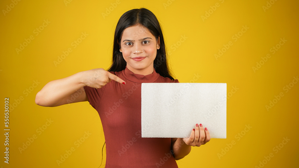 Beautiful young woman holding and pointing finger at empty blank white board, your text here concept, Asian Indian girl isolated over colour background studio Beautiful young woman holding and pointing finger at empty blank white board, your text here concept, Asian Indian girl isolated over colour background studio