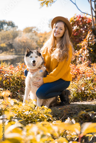 Girl sitting with husky dog in the autumn park