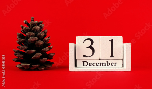 Photography Large Christmas tree cone and wooden calendar with the date December 31 on a red