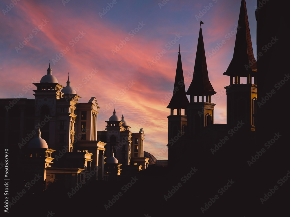 View of several black silhouettes of historic palace towers against a sunset orange sky and a sunbeam