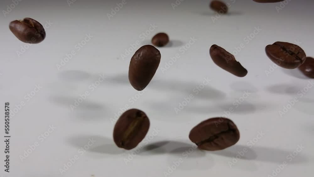 Close-up of aromatic roasted coffee beans falling and bouncing on white surface