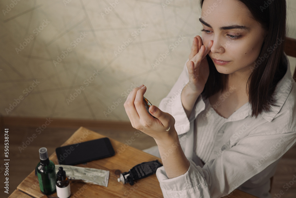 High angle of tender woman delicately applying facial cream during skin care beauty treatment while looking in mirror at home High angle of tender woman delicately applying facial cream during skin care beauty treatment while looking in mirror at home