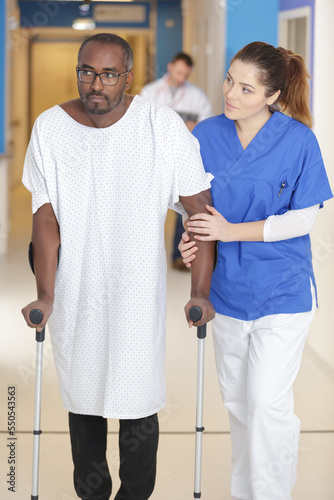 physiotherapist assisting injured young male patient walking with crutches