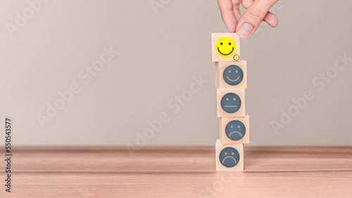 Hand putting a wooden cube block with a smile face icon on wood table. Concept of customer services best excellent business rating experience and testimonial.