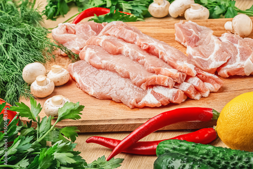 Fresh pork meat steaks on a wooden board. Mushrooms, tomatoes, lemon, parsley, dill and cucumbers. Ingredients for the recipe. Close-up. Fresh pork meat steaks on a wooden board. Mushrooms, tomatoes, lemon, parsley, dill and cucumbers. Ingredients for the recipe. Close-up.