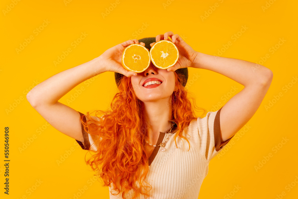 Redhead woman holding an orange over isolated yellow background covering eyes smiling