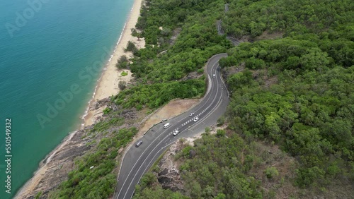 Aerial video of drone flying forward and camera paning up showing tropical road with beaches and mountains