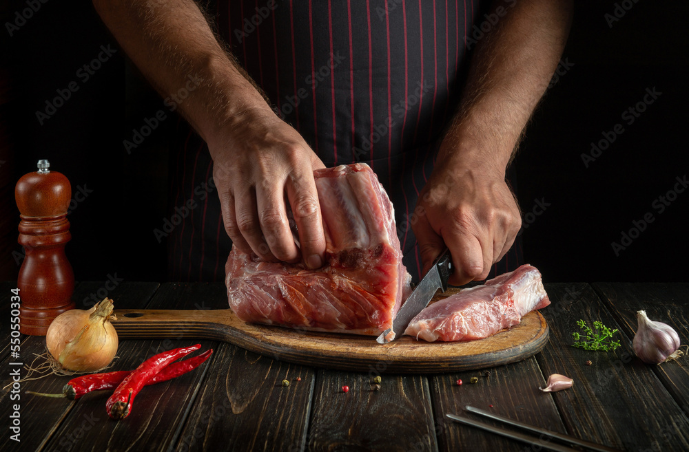 Chef cuts raw ribs on a cutting board before baking. Cooking delicious food in the kitchen. Delicious grill idea