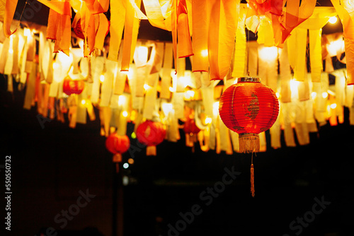 Chinese paper red lanterns hang with garlands of ribbons and lamps at night in the yard