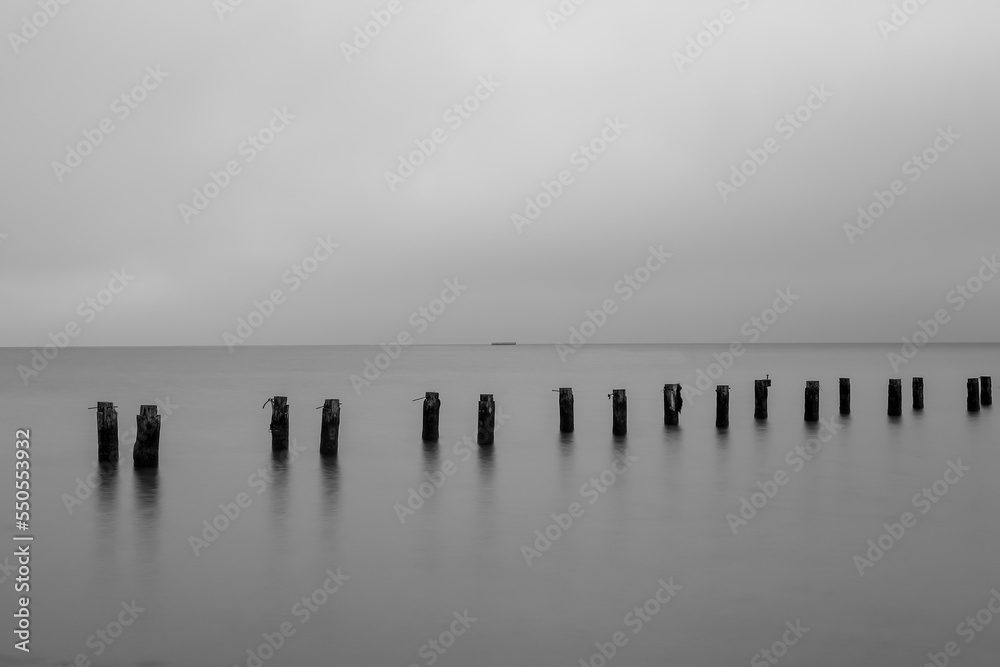Fototapeta premium The ruins of an old pier sticking out of the water in Gdynia, Poland, in black and white