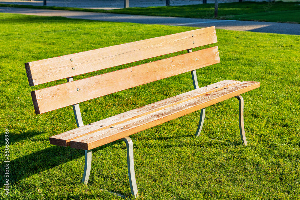 Close-up of an empty wooden park bench on green grass. Malcesine village, tourist resort on the coast of Lake Garda (Lago di Garda), Veneto, Italy, Europe. Close-up of an empty wooden park bench on green grass. Malcesine village, tourist resort on the coast of Lake Garda (Lago di Garda), Veneto, Italy, Europe.