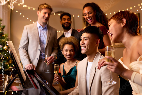 Group Of Friends Around Piano Celebrating At Christmas Or New Year Party Together