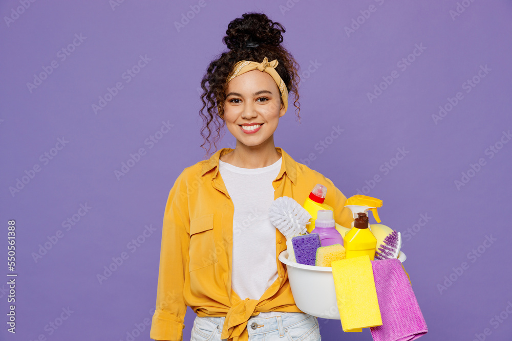 Young smiling happy fun housekeeper woman in yellow shirt while doing housework tidy up hold basin with detergent bottles isolated on plain pastel light purple background studio Housekeeping concept Young smiling happy fun housekeeper woman in yellow shirt while doing housework tidy up hold basin with detergent bottles isolated on plain pastel light purple background studio Housekeeping concept