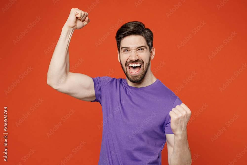 Young fun brunet caucasian man 30s wear casual basic purple t-shirt doing winner gesture celebrate clenching fists say yes isolated on plain orange background studio portrait People lifestyle concept Young fun brunet caucasian man 30s wear casual basic purple t-shirt doing winner gesture celebrate clenching fists say yes isolated on plain orange background studio portrait People lifestyle concept
