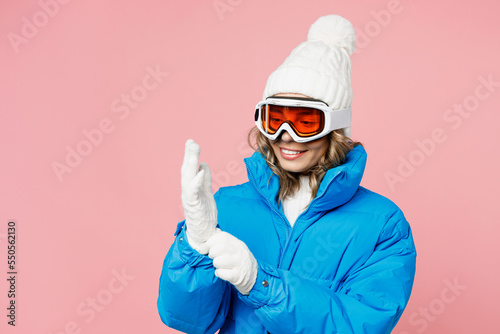 Snowboarder smiling fun cheerful woman wear blue suit goggles mask hat ski padded jacket put on gloves isolated on plain pastel pink background. Winter extreme sport hobby weekend trip relax concept