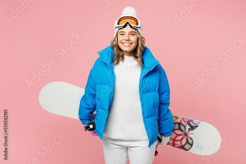 Snowboarder happy woman wear blue suit goggles mask hat ski padded jacket hold snowboard behind herself isolated on plain pastel pink background. Winter extreme sport hobby weekend trip relax concept.