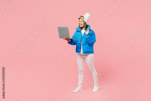 Snowboarder IT woman wear blue suit goggles mask hat ski jacket work hold use laptop pc computer waving hand isolated on plain pink background. Winter extreme sport hobby weekend trip relax concept.