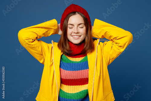 Young woman in sweater red hat yellow waterproof raincoat outerwear hold folded hands behind neck close eyes isolated on plain dark royal navy blue background Outdoor wet fall weather season concept © ViDi Studio