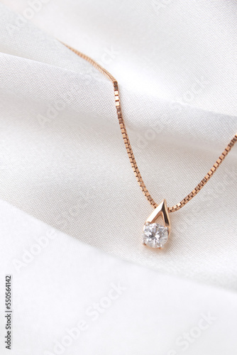 Golden necklace with crystals on white silk background, rose gold, single diamond pendant. Beautiful accessories for women. Elegant jewelery gift or present for wedding or saint valentine's day.