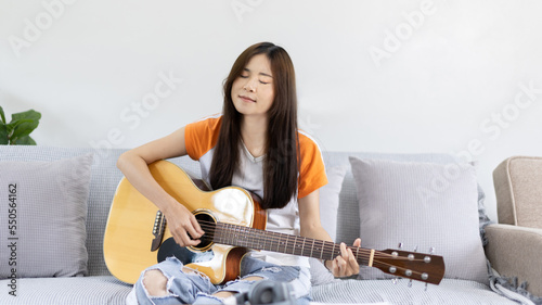 Asian female artist playing the guitar and singing happily in the living room, Relaxation with music therapy, Spending free time with music, Joy of playing music, Acoustic guitar.