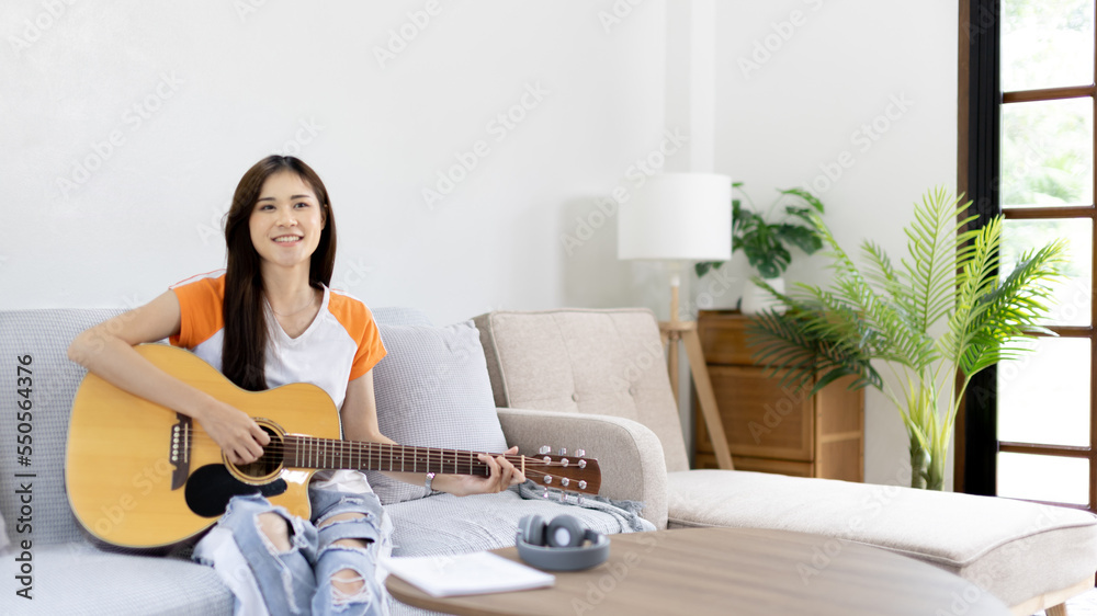 Asian female artist playing the guitar and singing happily in the living room, Relaxation with music therapy, Spending free time with music, Joy of playing music, Acoustic guitar. Asian female artist playing the guitar and singing happily in the living room, Relaxation with music therapy, Spending free time with music, Joy of playing music, Acoustic guitar.