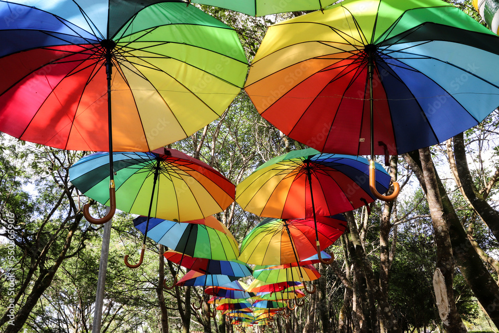 colorful hanging umbrellas, forming a corridor amidst trees and blue sky
