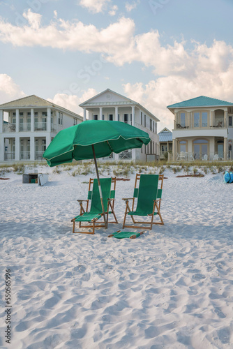 Destin, Florida- Green outdoor lounge chairs under the umbrella on a white beach sand © Jason
