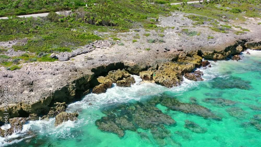 overhead aerial of turquoise blue waves crashing onto sharp rocks on Cozumel Island in Mexico