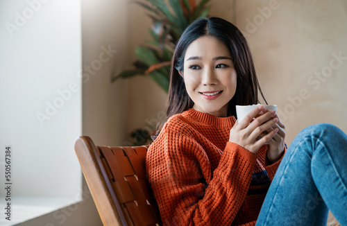 Картината върху платно Portrait of young beautiful asian woman in sweater hands holding a cup of marsh mellow coffee morning winter time relax at home