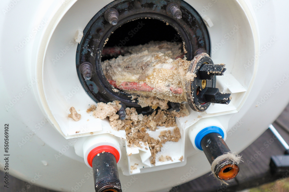 Water heater repair. Repair and maintenance of boilers. The master plumber  pulls out a tubular electric heater covered with lime scale from the hole  in the boiler. Photos | Adobe Stock