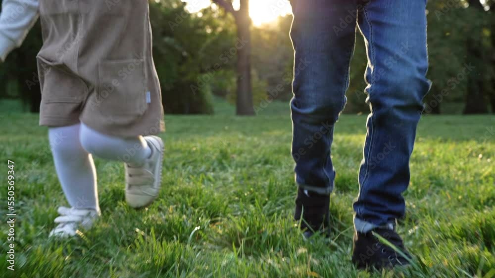 Children's feet run on the green grass in the park. Walk at sunset. Children's feet run on the green grass in the park. Walk at sunset.