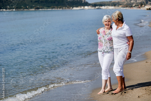 coppia di signore anziane camminano divertite in spiaggia sulla riva del mare