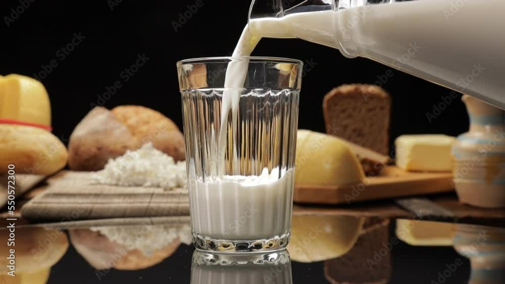 Natural rustic products: pieces of cheese on a wooden board, bread and a glass into which milk is poured from a jug.