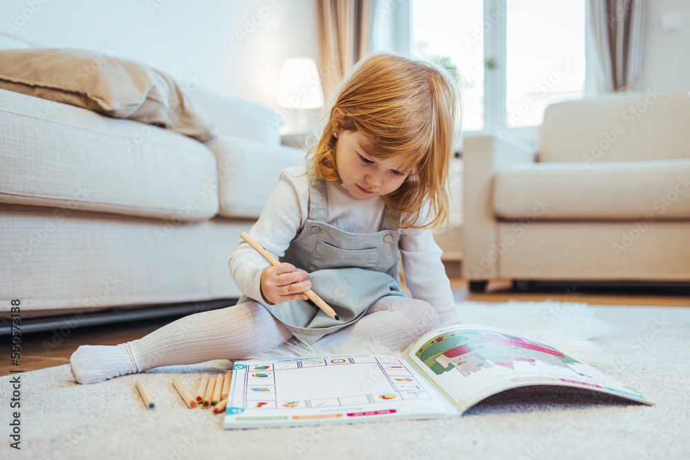Kindergarten children education, or preschool child study at home concept. Close up photo of a blonde little girl drawing something in her notebook sitting at the table in the kitchen Kindergarten children education, or preschool child study at home concept. Close up photo of a blonde little girl drawing something in her notebook sitting at the table in the kitchen