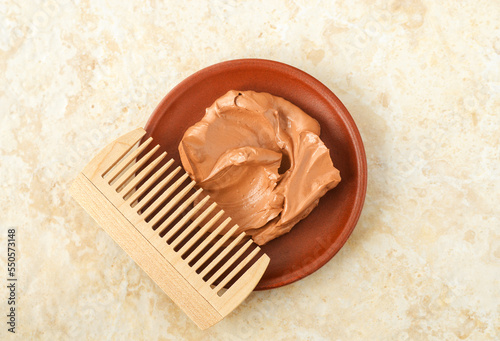 Red moroccan bentonite clay in a small ceramic bowl and wooden hairbrush (comb). Diy facial or hair mask, body wrap recipe. Natural beauty treatment and spa. Top view.