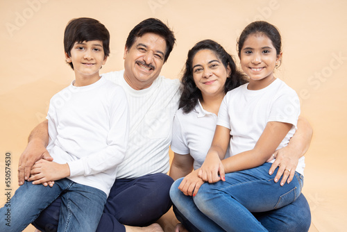 Happy indian grandparents with kids wearing white casual t-shirt sitting together isolated over beige background.