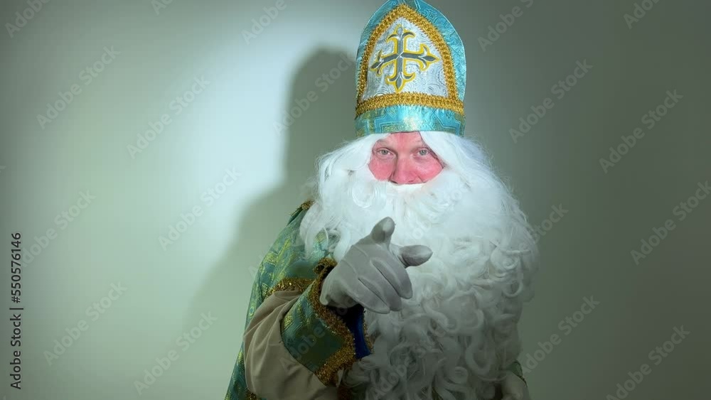 he has a turquoise and gold suit long white beard and a hat with Sinterklaas portrait Dutch Santa Claus St Nicholas christmas new year walks slowly and looks into the frame points his finger at us
