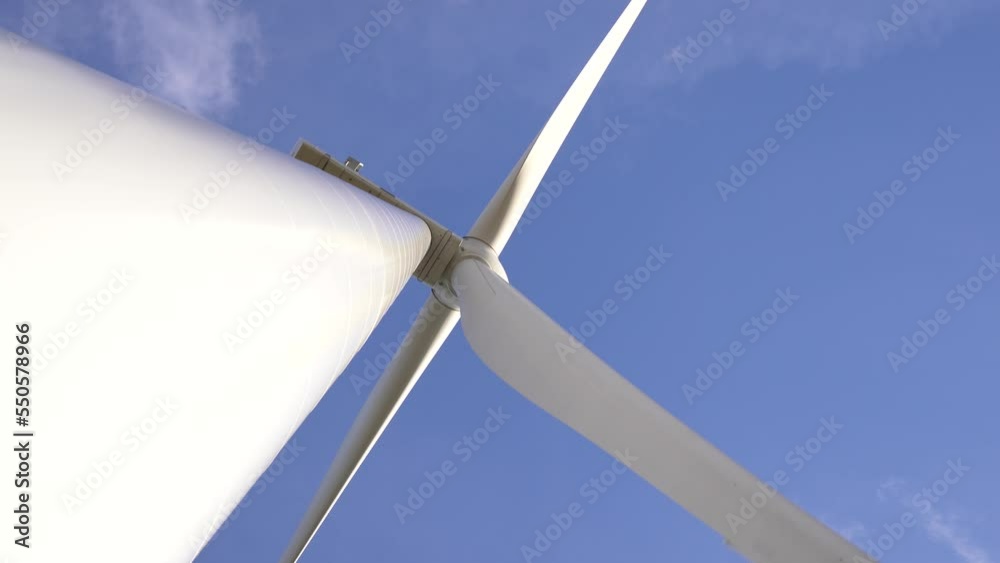 Blades of a Large Wind Turbine in a Field Against Blue Sky. View from the bottom up. Alternative Energy Sources - Ecological energy. Blades of a Large Wind Turbine in a Field Against Blue Sky. View from the bottom up. Alternative Energy Sources - Ecological energy.