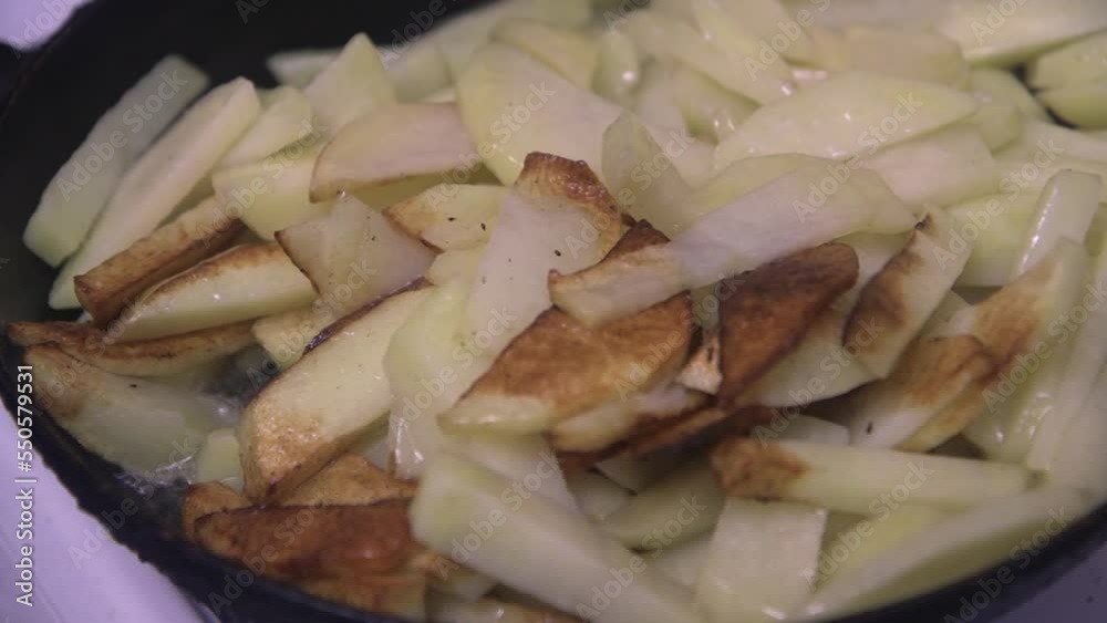 a wooden spoon stirs the chopped potatoes in a frying pan, close-up, top view a wooden spoon stirs the chopped potatoes in a frying pan, close-up, top view
