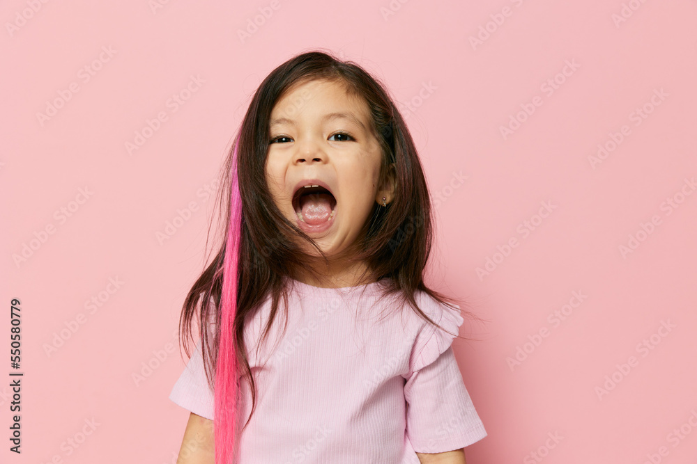 a beautiful little girl of preschool age stands on a pink background in a pink T-shirt and looks thoughtfully away smiling shyly holding her finger near her lips a beautiful little girl of preschool age stands on a pink background in a pink T-shirt and looks thoughtfully away smiling shyly holding her finger near her lips