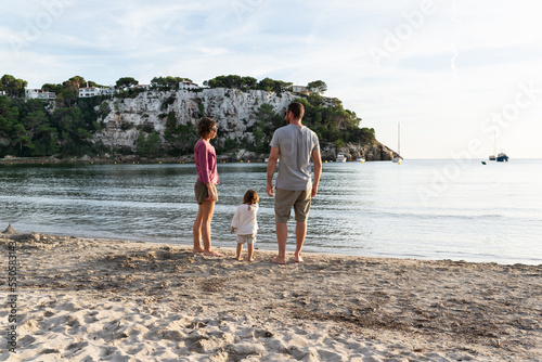 Mother, father and their little daughter enjoying the sunset at a nice sand beach called cala Galdana located in Menorca, spain. photo