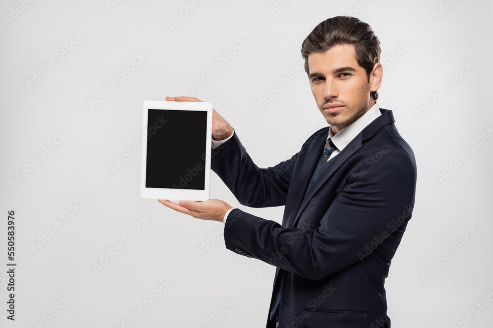 young businessman in suit holding digital tablet with blank screen isolated on grey young businessman in suit holding digital tablet with blank screen isolated on grey