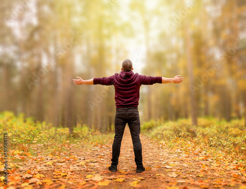A relaxed adult man is standing on a path in the autumn forest  breathing fresh air. The arms are spread apart