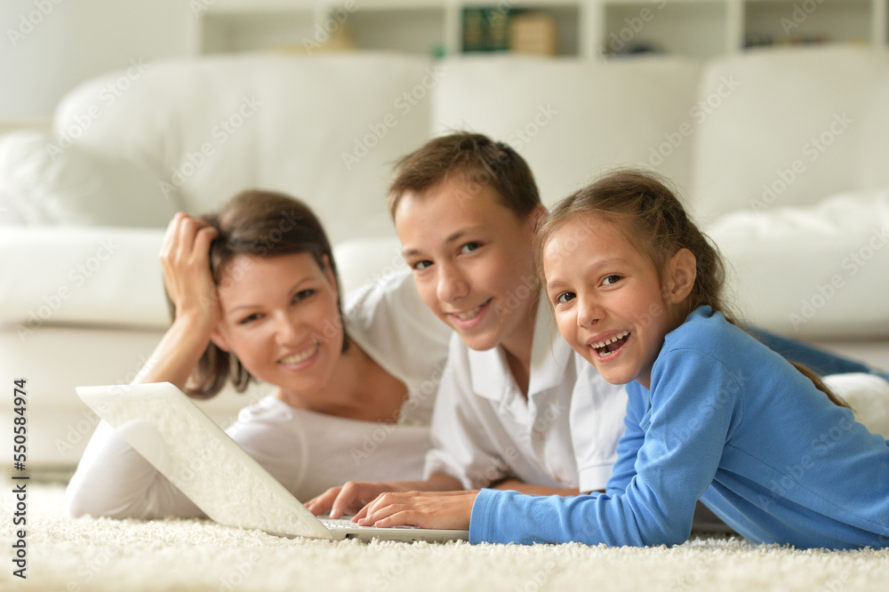 mom and kids are lying with a laptop on the carpet