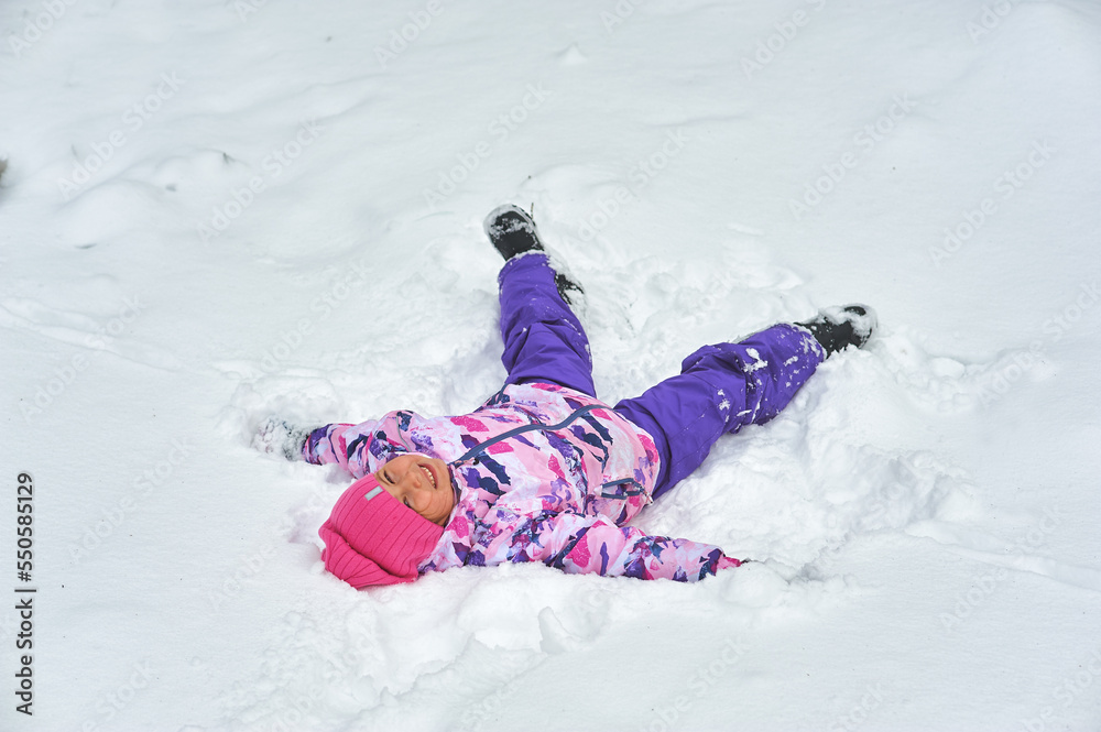 Happy little girl rejoices in winter lying on the snow