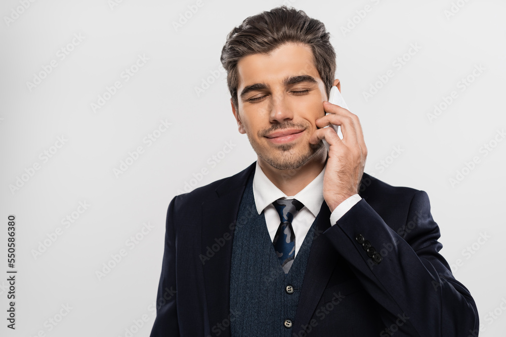 pleased businessman in suit standing with closed eyes and talking on smartphone isolated on grey pleased businessman in suit standing with closed eyes and talking on smartphone isolated on grey