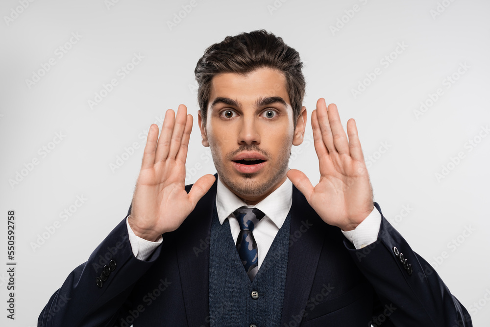 surprised businessman in suit gesturing while looking at camera isolated on grey surprised businessman in suit gesturing while looking at camera isolated on grey