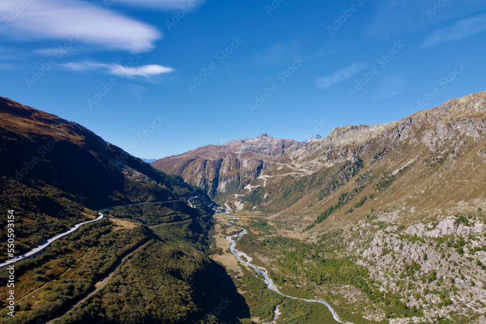 Mountain panorama with Rhone River in the Swiss Alps at region of mountain pass Furkapass with serpentine road of Grimselpass in the background. Photo taken September 12th, 2022, Goms, Switzerland.